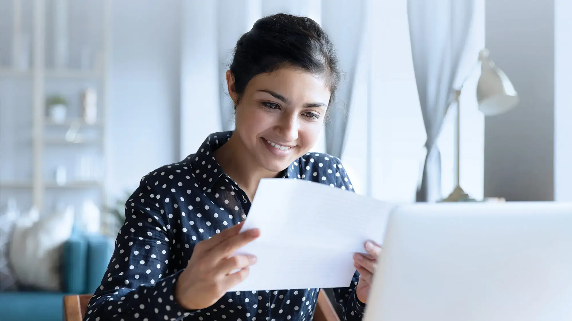 Person sitzt am Laptop und hält ein Dokument in der Hand