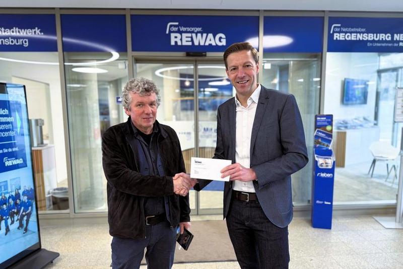 REWAG-Sprecher Martin Gottschalk übergibt einen Scheck über 1.500 Euro an Sepp Zauner. Er leitet Kleinkunstbühne in Tom’s Bar im Thomas-Wiser-Haus.