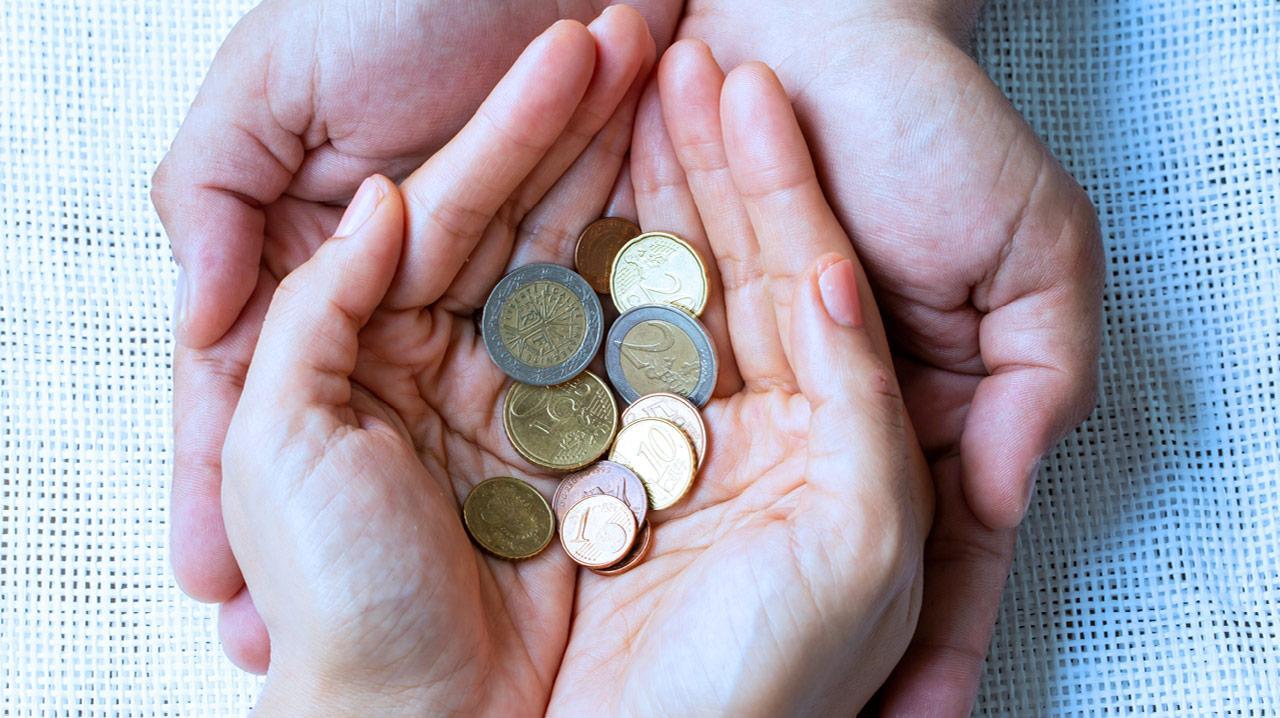 Zwei Hände, eine größere und eine kleinere, halten mehrere Euro-Münzen unterschiedlicher Werte.