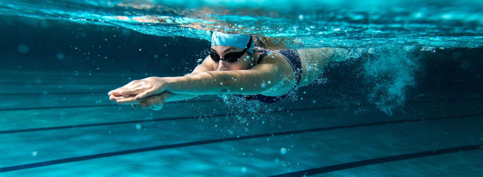 Schwimmerin mit Schwimmbrille und Haube unter Wasser im Schwimmbecken