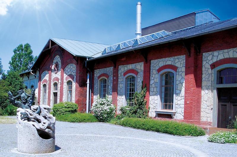 Historisches Maschinenhaus im Wasserwerk Sallern. Backsteingebäude mit Steinfassade, Innenhof und Natursteinbrunnen auf gepflastertem Platz.