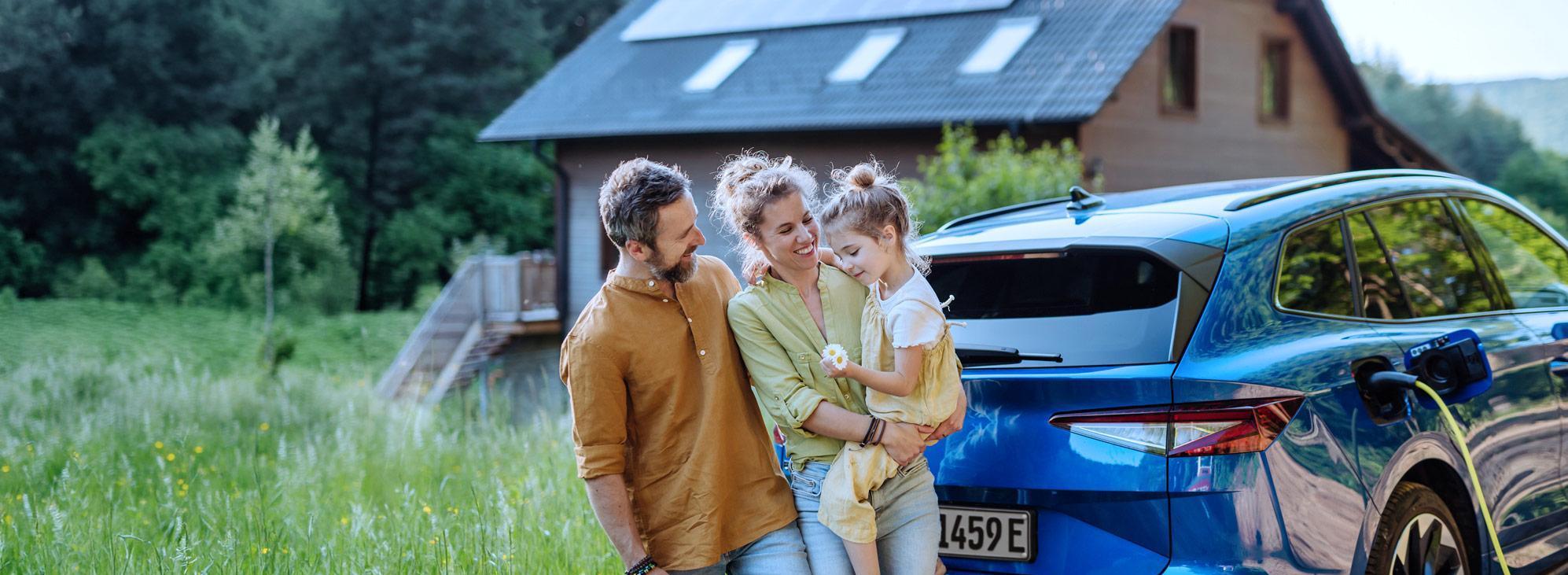 Junge Familie steht vor Einfamilienhaus und lädt das E-Auto