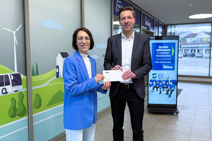 REWAG-Sprecher Martin Gottschalk übergibt einen Scheck über 1.000 Euro an Magdalena Plank. Sie organisiert mit ihrem Verein ein Matsch- und Hindernisrennen.