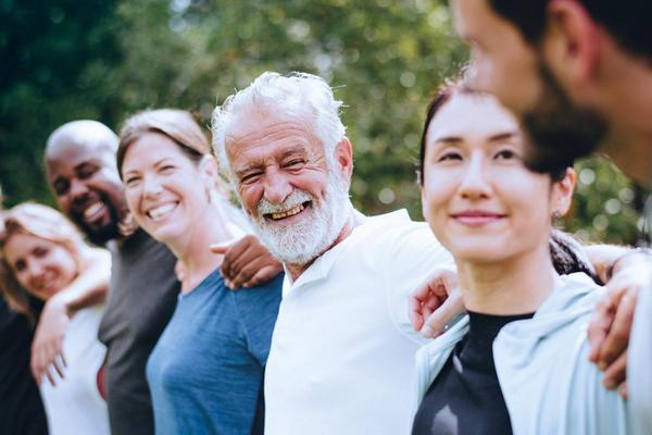Gruppe von Menschen steht eng nebeneinander im Freien vor grünen Bäumen.