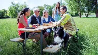 Eine Gruppe fröhlicher Vereinsmitglieder zusammen an einem Tisch im Freien
